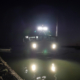 Front view of a boat by a dock at night, lights on flashing at camera